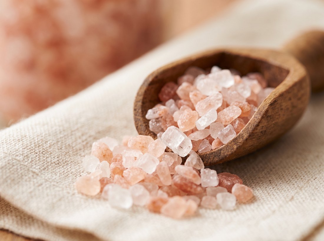 Gros plan sur des cristaux de sel rose de l'Himalaya versés d'une cuillère en bois sur un tissu de lin